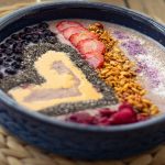 Vibrant smoothie bowl with fresh fruits and seeds on a woven placemat, perfect for a healthy breakfast idea.