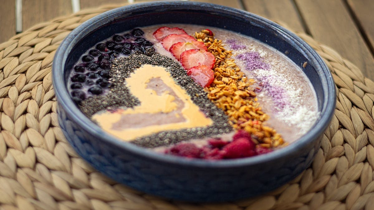Vibrant smoothie bowl with fresh fruits and seeds on a woven placemat, perfect for a healthy breakfast idea.
